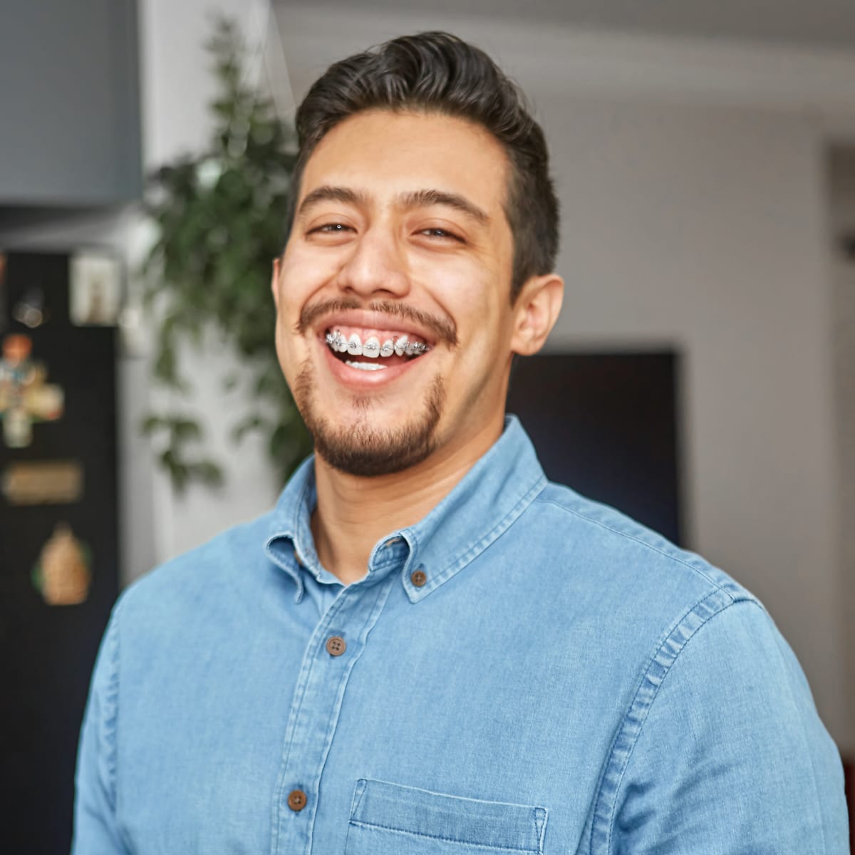 A man with short hair and braces is standing inside a house smiling.