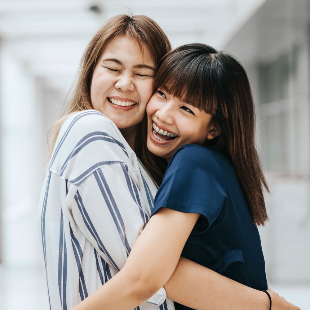 Two young women smile while embracing eachother.