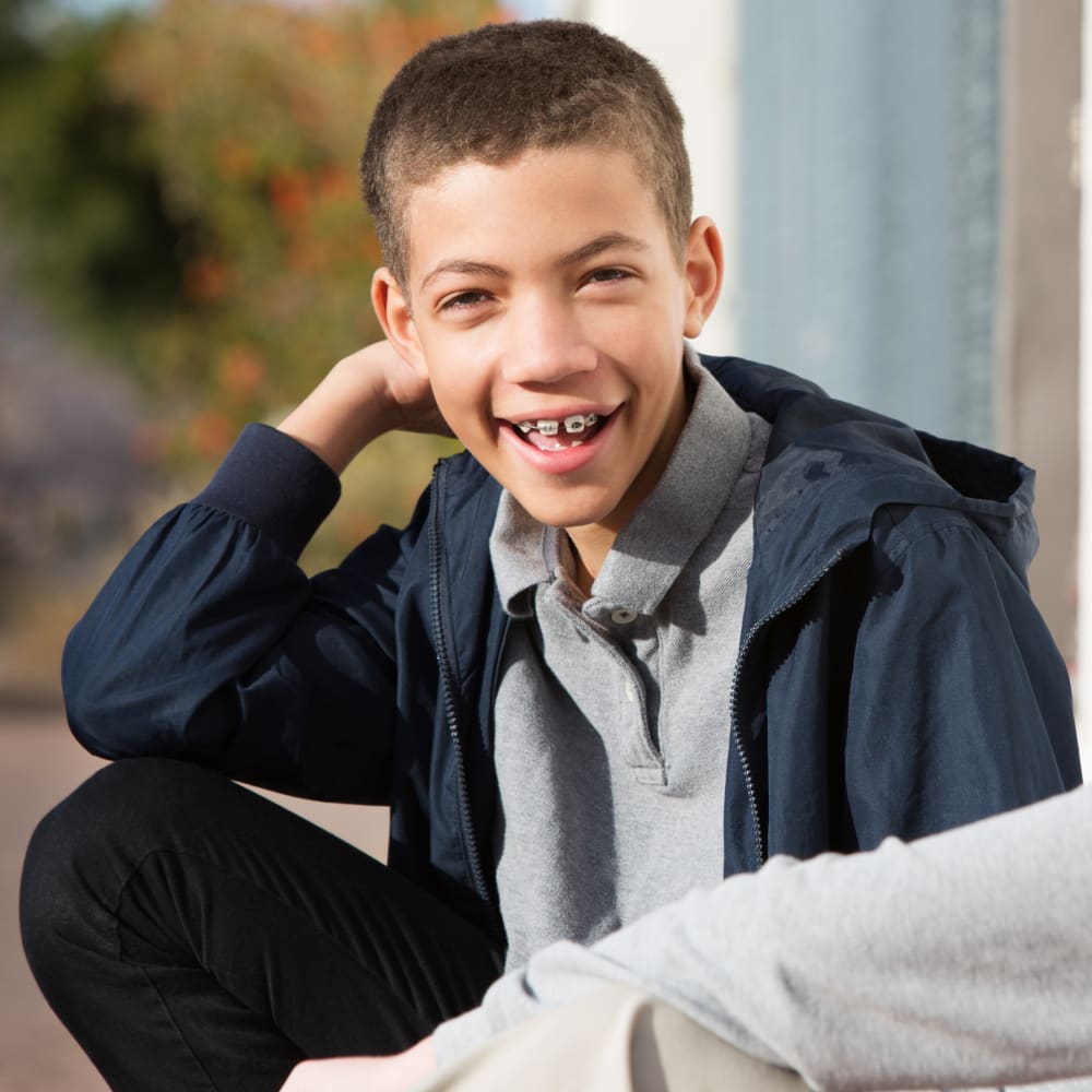 A young boy with braces is sitting outside smiling.