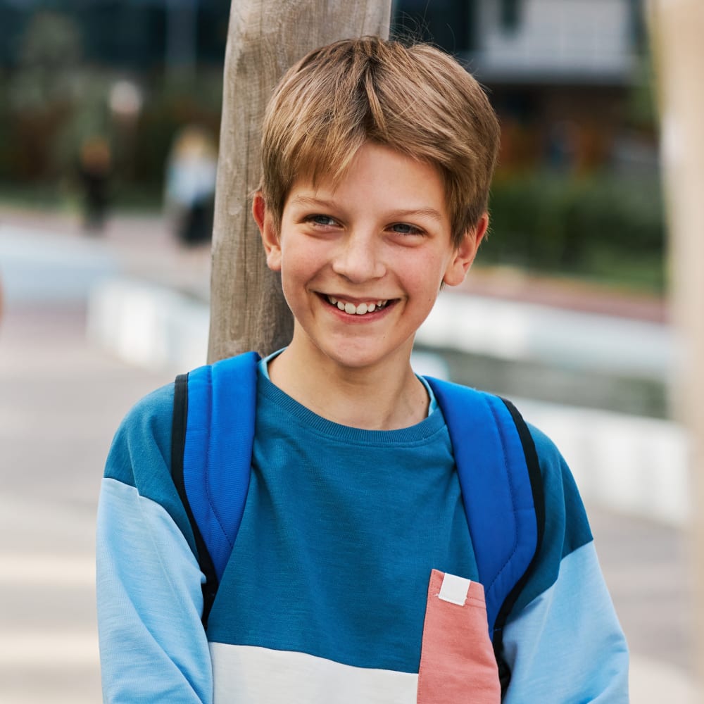 A young boy is standing outside with a backpack on and smiling.