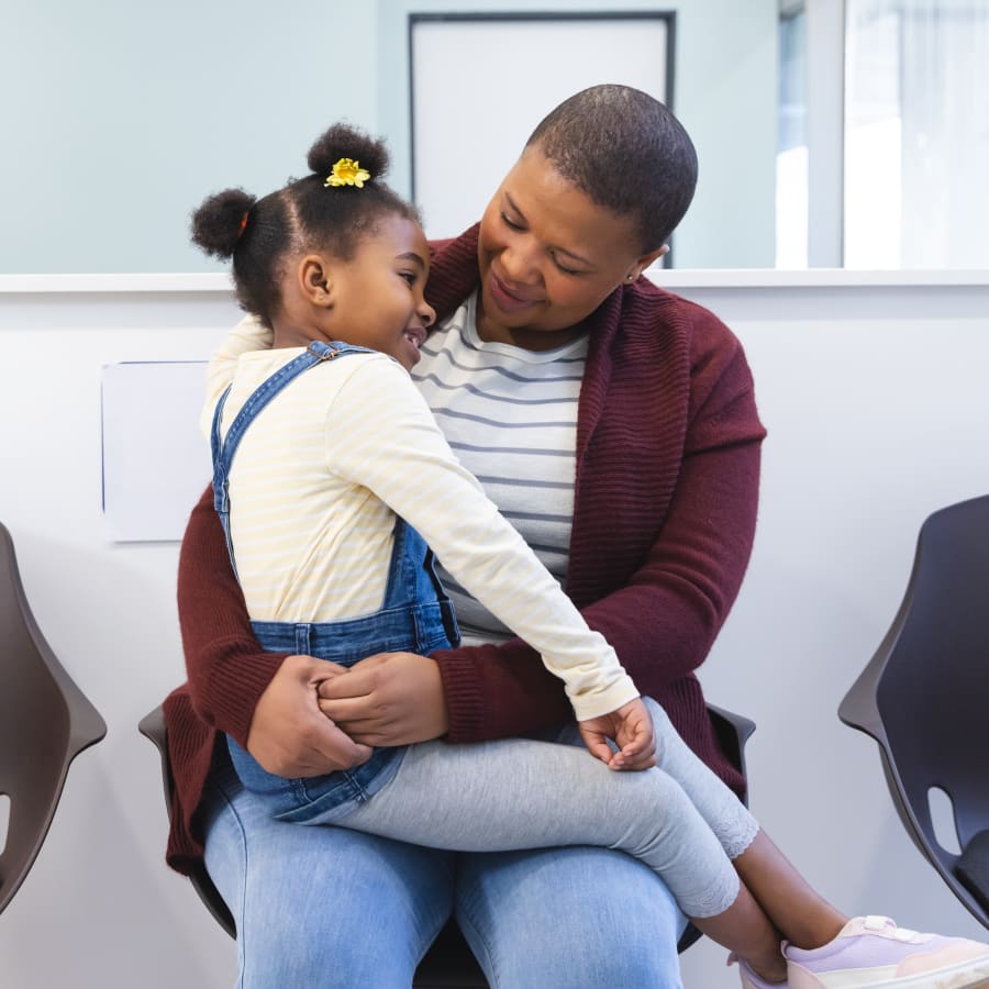 A child sits on her mother's lap in a waiting room.
