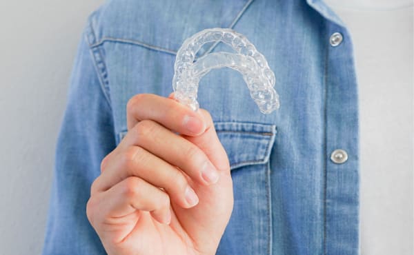 A person out of frame is holding up a pair of clear aligners.