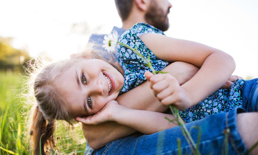 A woman smiles at a child she is carrying on her back.