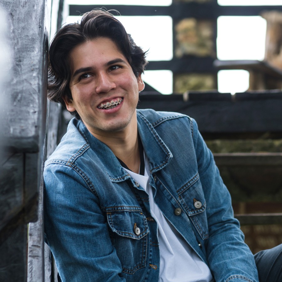 A teenage boy with braces is sitting outside smiling.
